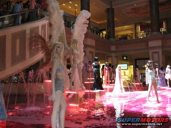mannequins dressed in sparkly outfits and lingerie displayed around a pink fountain in a mall