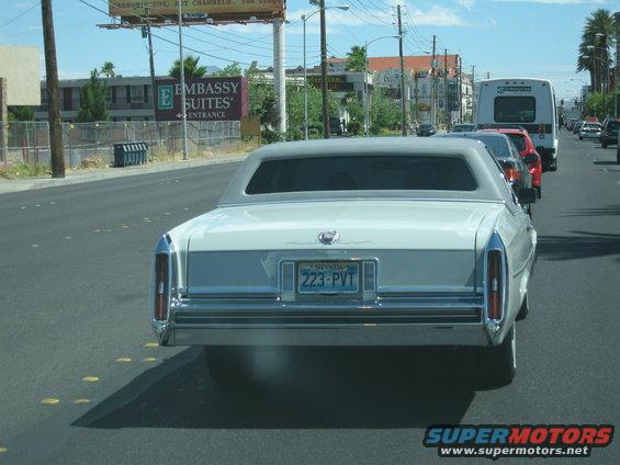 White Cadillac sedan driving on a road, Nevada license plate 223-PVT