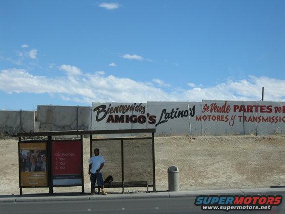 Bus stop with 'Bienvenidos Amigo's Latino's' and 'Se Vende Partes de Motores y Transmision' murals on a concrete wall