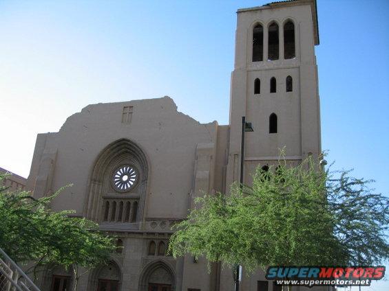 Tan church building with a bell tower and a rose window under a clear blue sky