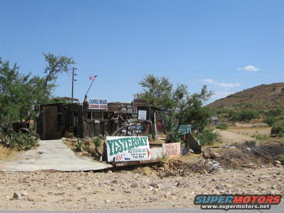 dilapidated buildings with signs for Candle Shack and Yesterday Restaurant in a desert landscape