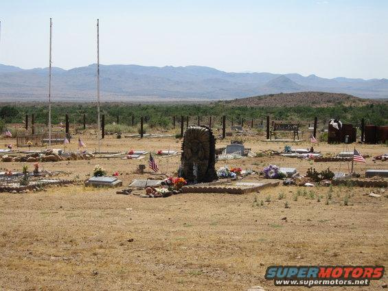 Desert cemetery with graves and flags under a clear sky