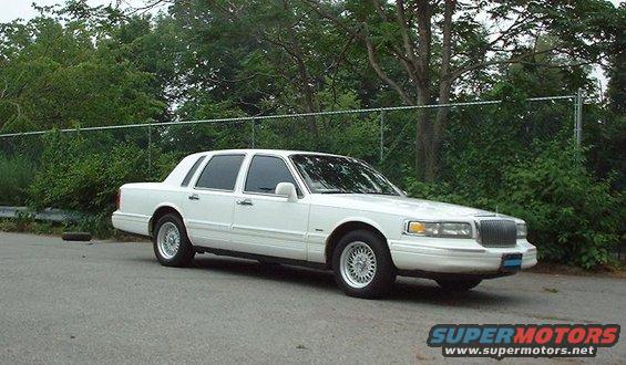 White Lincoln Town Car parked on asphalt with trees and a fence behind it