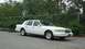 1997 Ford Crown Victoria - This white Lincoln Town Car is parked on a paved surface with a chain-link fence and trees in the background.
