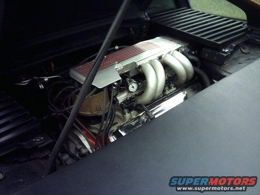 Engine bay with chrome exhaust manifolds and a gauge visible