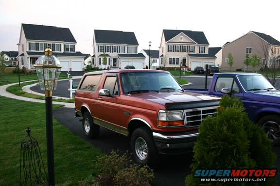 Red Ford Bronco parked in driveway, front 3/4 view. Grille and headlights visible