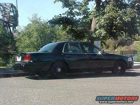 Black sedan parked on street, trees and bridge in background