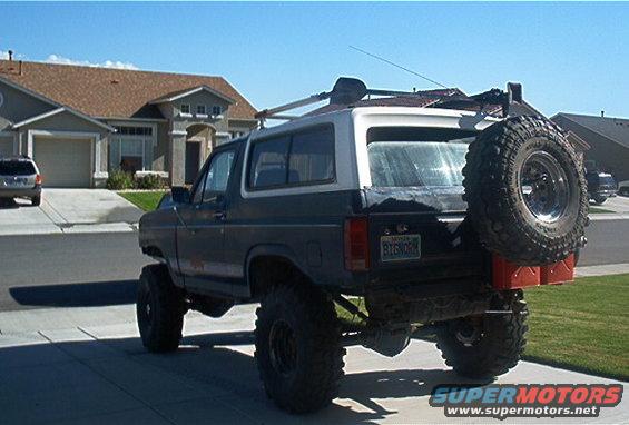 1986 Ford Bronco lifted with large tires, spare tire on rear carrier, and red gas cans