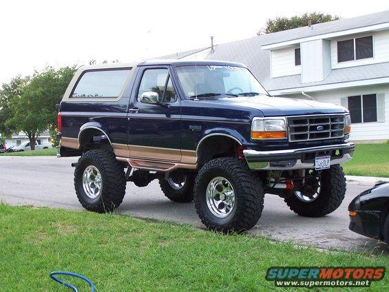 Blue 1995 Ford Bronco with tan trim and lifted suspension, parked on a residential street