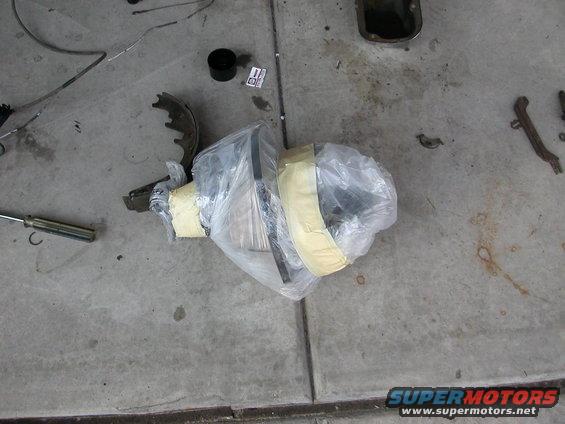 Differential and brake parts wrapped in plastic on concrete floor. Screwdriver nearby