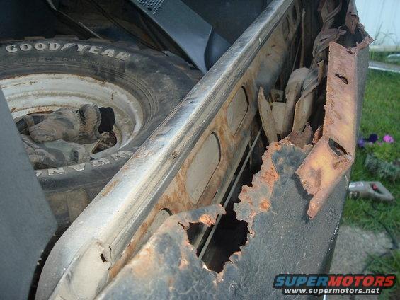 Spare tire visible next to heavily rusted vehicle frame section