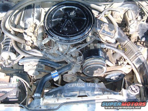 Engine bay with air cleaner, belts, and radiator visible. Text 'CAUTION FAN' on shroud