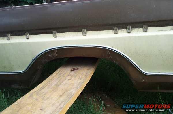 Two-tone brown and tan vehicle rear wheel well with chrome trim, supported by a wooden plank