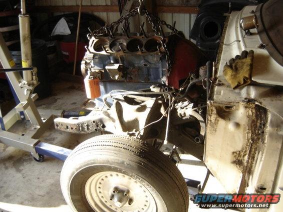Engine hoist lifting engine out of a car chassis, showing front wheel and frame