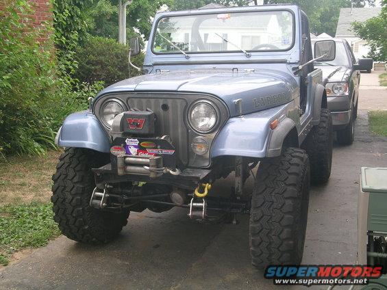 Blue Jeep CJ-7 Laredo with winch, lifted suspension, and large tires parked in front of a pickup truck