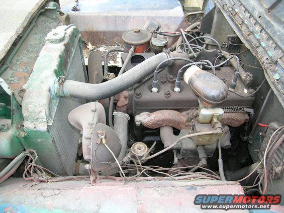 Engine bay of an old vehicle, showing the radiator, engine block, spark plug wires, and hoses