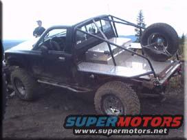 Black modified pickup truck with roll cage, flatbed, and spare tire mounted on the back