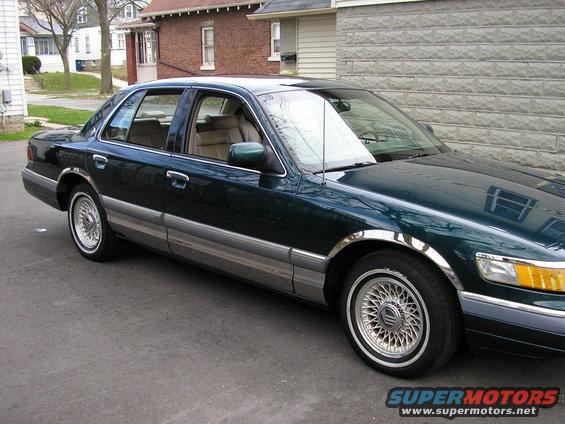 Dark green sedan parked on asphalt, 3/4 front view. Chrome trim, wire wheels, tan interior visible
