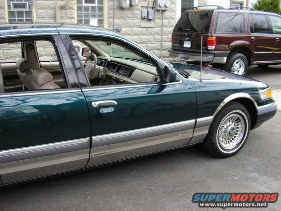 Side view of a dark green sedan with chrome trim. A maroon SUV is parked behind it