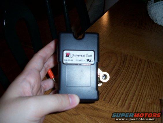 Hand holding black electronic module with 'Universal Tool' label. Orange wire attached