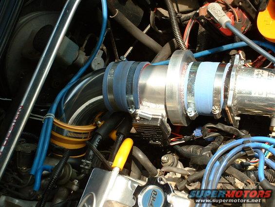 Close-up of engine bay showing a modified intake system with blue hoses and metal piping