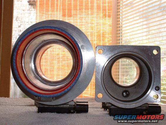 Two automotive throttle bodies, one round and one square, sit on a surface in front of a window with blinds