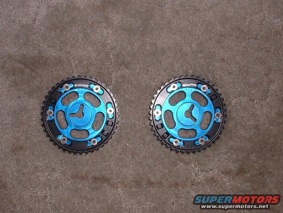 Two blue adjustable camshaft gears with black outer rims and silver bolts, lying on a concrete surface