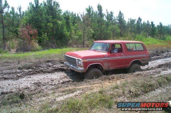 Red SUV stuck in mud, front 3/4 view. Visible grille and side trim