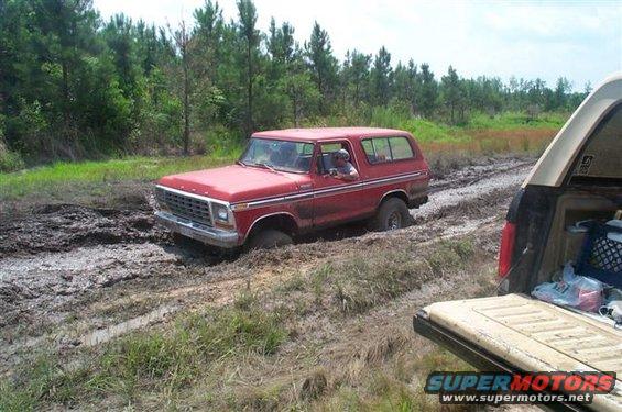 Red 1978 Ford Bronco stuck in mud, with another vehicle's tailgate visible