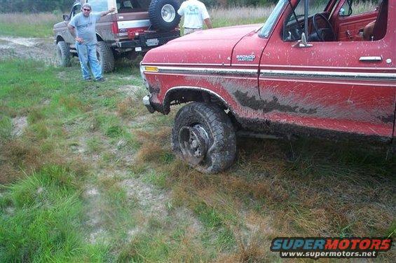 Muddy red Ford Bronco with flat tire, another brown Ford truck behind it