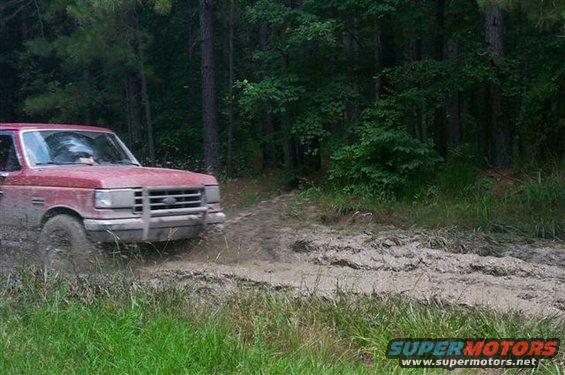 Red Ford F-Series truck driving through a muddy trail in the woods