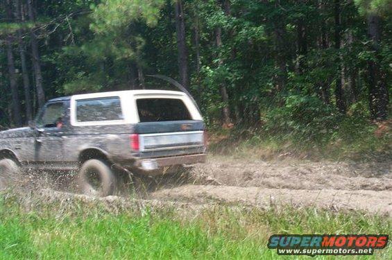 Muddy Ford Bronco driving off-road, kicking up dirt