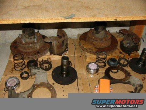 Disassembled front brake rotors, calipers, hubs, and springs laid out on a wooden surface