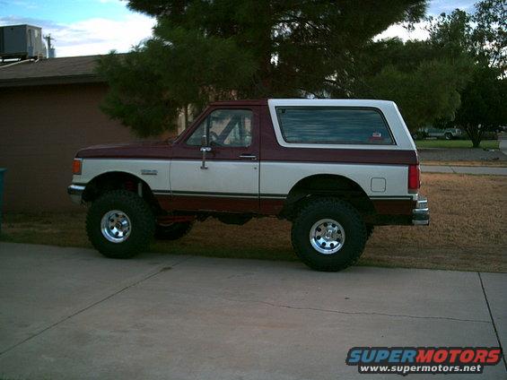 Maroon and white Ford Bronco lifted with big tires, parked on a driveway