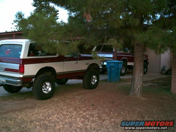 Maroon and white Ford Bronco with large tires parked next to a red pickup truck