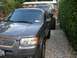1994 Ford Bronco - A gray Ford Escape is parked in front of a lifted black Ford Bronco with custom tires.