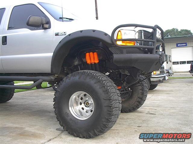 Silver pickup truck with oversized tires, black fender flares, and a black brush guard over the front grille and headlights