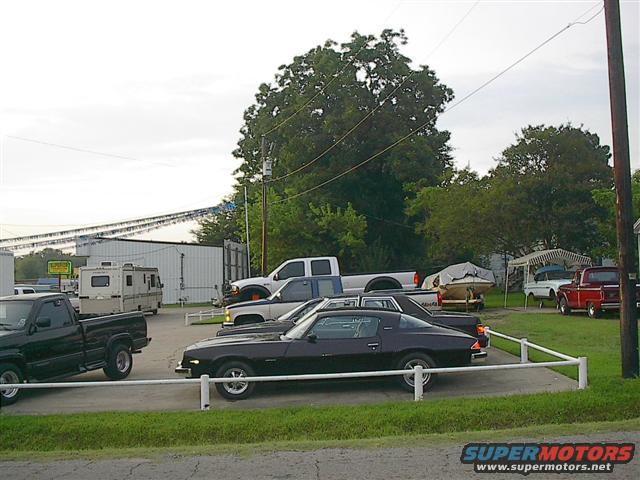 Black coupe with a white stripe on the side, parked on asphalt with a white railing. Visible wheels and side profile