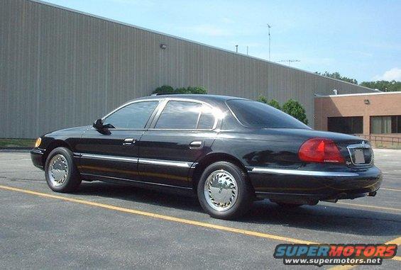 Black sedan parked in a lot, rear three-quarter view. Chrome trim and hubcaps visible