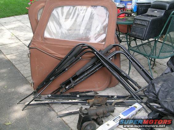 Brown Jeep soft top with frame and assorted parts on pavement