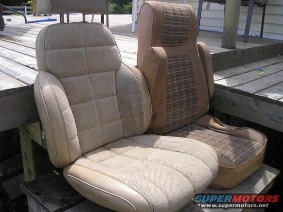 Two tan car seats with patterned fabric inserts, one with a headrest, sitting on a wooden deck