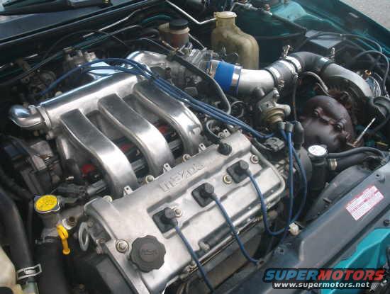 Engine bay of a 1994 Mazda MX-3, showing the V6 engine with aluminum intake manifold and blue spark plug wires