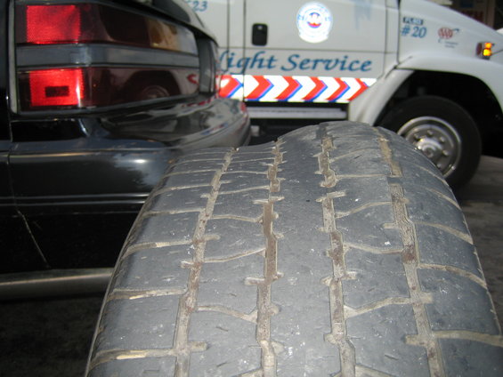 Worn tire in foreground, rear of black car, and white service van with text 'Light Service'