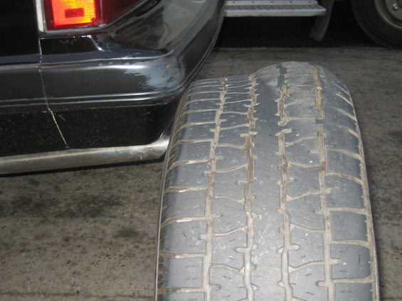 Close-up of a worn tire tread next to the black bumper and taillight of a car