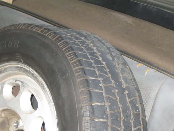 Spare tire with a silver rim and a worn tread pattern, next to a grey interior panel