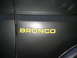1986 Ford Bronco - Close-up of a yellow Bronco emblem affixed to the side of a vehicle.