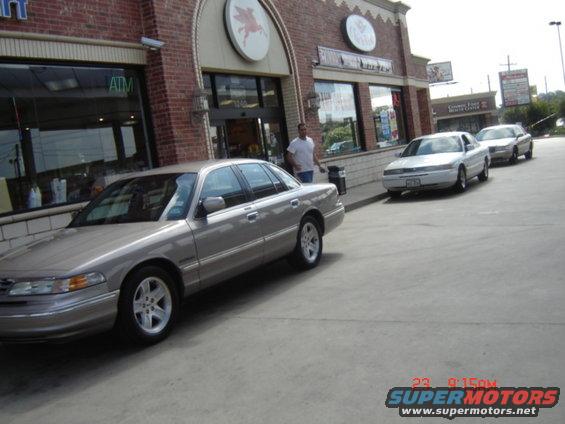 Silver Ford Crown Victoria parked in front of a building with two other cars behind it
