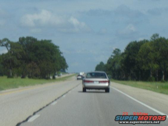 Car driving on a highway with trees on both sides. Another car is ahead