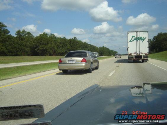 Gold sedan with a license plate visible, driving on a highway next to a white semi-truck