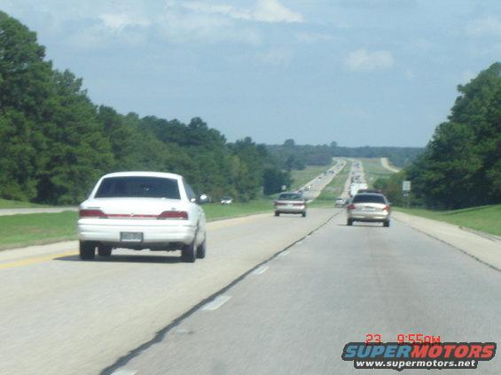 Multiple cars driving on a highway with trees lining the sides